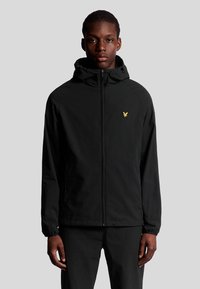 Veste noire à fermeture éclair avec capuche, fabriqu�ée en matériau léger. Présente un logo doré sur la poitrine gauche, des poignets élastiques et un design simple.