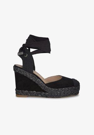 Black wedge sandal with a woven jute base, soft suede upper, and ankle wrap. Features a rounded toe and textured fabric straps.