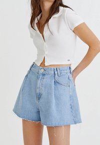 Top corto blanco acanalado con mangas cortas, combinado con pantalones cortos de mezclilla azul claro de cintura alta, con bajos deshilachados y bolsillos delanteros.