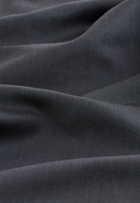 Tessuto grigio scuro con una superficie liscia e leggermente strutturata, che mostra leggere pieghe e grinze, indicative di peso e fluidità.