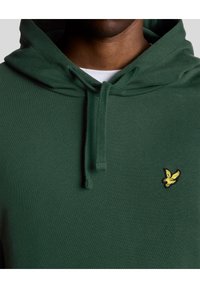 Felpa verde con tasca a kangaroo frontale, cappuccio con lacci e logo giallo ricamato sul petto sinistro. Tessuto morbido e testurizzato.