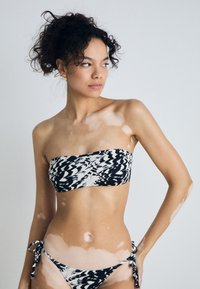Bikini i sort-hvitt mønster med bandeau-overdel, som har bånd i sidene, glatt stoff og en tettsittende design som fremhever kurvene.