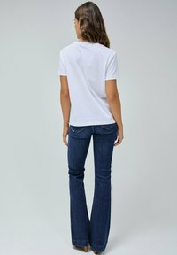 T-shirt blanc à manches courtes associé à un jean évasé bleu marine. Les jeans présentent des poches arrière avec des détails de couture subtils.