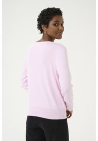 Maglione lungo rosa chiaro a maniche lunghe con scollatura rotonda e bordo a costine, realizzato in materiale morbido, mostrato indossato di spalle.