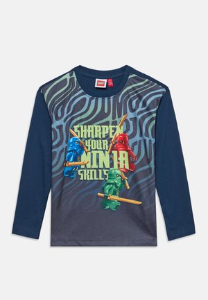 Chemise bleu marine à manches longues avec des figurines LEGO ninja en bleu, rouge et vert tenant des épées et le texte "Sharpen Your Ninja Skills" sur le devant.
