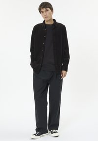Mørkebrun corduroy skjorte i button-down stil. Bæres over en sort crew-neck skjorte, sammen med løse sorte bukser og sorte sneakers.