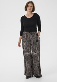 Top nero aderente abbinato a pantaloni palazzo con un motivo ondulato in nero e rosa. I pantaloni hanno una vita elastica e tasche.