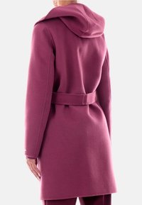 Cappotto di lana magenta con cappuccio, vita con cintura e maniche lunghe. Texture soffice, taglio dritto e dettagli di cucitura minimi ai polsini.