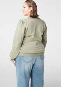 Lichtgroene, metallic textuur trui met pofmouwen, geribde manchetten en zoom, gecombineerd met lichtblauwe jeans met brede pijpen.