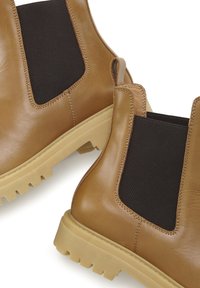 Bruine leren Chelsea boots met elastische zijkanten, stevige beige zool en contrasterende zwarte accenten aan de zijkanten.