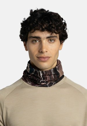 Young man with curly dark hair wears a patterned neck gaiter and a beige textured long-sleeve shirt, looking straight ahead.