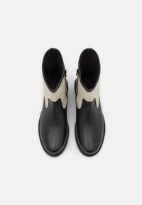 Botas de tornozelo em couro preto com um detalhe em tecido creme. Apresentam um fecho de zip com acabamento em ondas no tecido, exibindo uma textura suave.