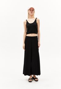 Zwart geribbeld crop top gecombineerd met zwarte wijde broek en zwarte platform sandalen. Model draagt een lichtroze pet, tegen een witte achtergrond.
