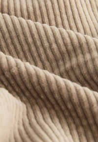Beige ribstof met een zachte, gestructureerde oppervlakte, gekenmerkt door uniforme verticale lijnen en een luxe uitstraling.