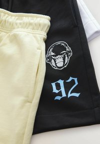 Svarta och gula shorts med elastisk midja. Det svarta tyget har en gorillagrafik och siffran "92" i ljusblått.