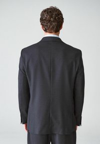 Dunkelgraue maßgeschneiderte Sakkokreation mit einer structurierten Silhouette, Reverskragen und einem Schlitz hinten. Glattes Gewebe mit Knopfakzenten.