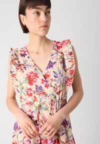 Rochie tip wrap floral din material crem, cu modele botanice vibrante în nuanțe de roșu, violet și verde. Are umeri volan și talie strânsă.