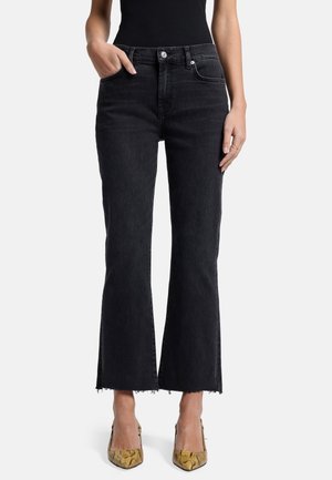 Jeans évasés noirs avec une finition brute, fabriqués en denim. Dotés de poches avant et d'une fermeture à bouton. Le modèle porte des talons en imprimé serpent.