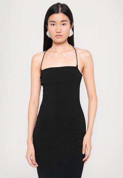 Black ribbed bodycon dress with thin straps, fitted design, and smooth texture. Model accessorized with white shell-shaped earrings.