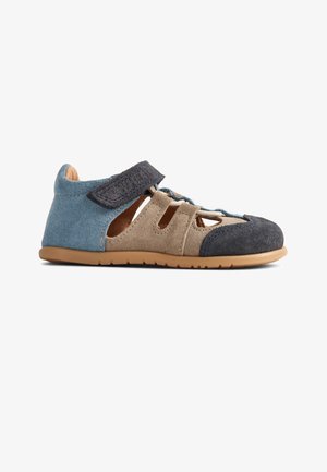 Chaussure en daim bleu et beige avec une semelle en caoutchouc, plusieurs découpes et une bride en Velcro pour une fixation sécurisée. Des accents texturés ornent le design.
