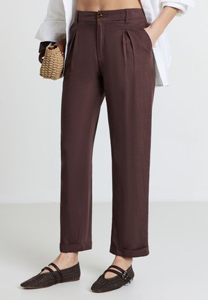 Pantaloni a pieghe marroni con una texture liscia, vita alta e chiusura con un solo bottone. Inclusi risvolti e tasche laterali.