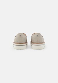 Beige sneakers with a textured upper, round heel, and white rubber sole featuring subtle brown accents and logo detail on the heel.