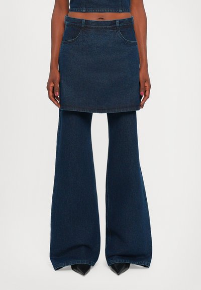 Dark denim skirt with a straight cut, front pockets, and a waistband. Paired with wide-leg dark denim pants and pointed black heels.