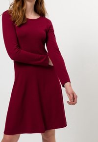 Vestido burdeos de manga larga, hecho de una tela suave, cuenta con un escote redondo y un dobladillo acampanado, con detalles de costura mínimos.