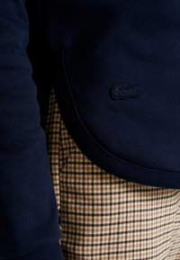 Mörkblå sweatshirt med en texturerad yta, med en broderad logotyp. I kombination med bruna och beige rutiga byxor.