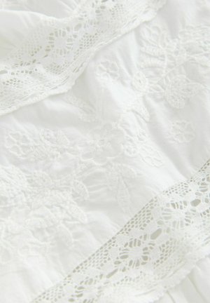 Țesătură albă cu broderie florală elaborată și dantelă delicată la margine. Textură moale cu elemente de design în straturi.