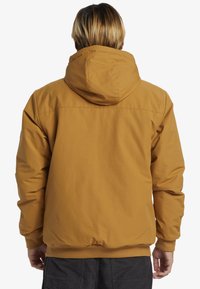 Chaqueta con capucha marrón de acabado suave y mate. Presenta puños elásticos, una capucha ajustable y un corte holgado.