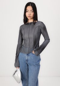 Gray long-sleeve top with a fitted design, featuring contrast stitching and an elongated shape, paired with light blue baggy jeans and a silver clutch.