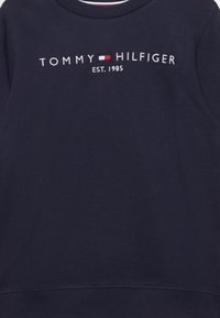 Granatowa bluza zwykła wykonana z mieszanki bawełny z okrągłym dekoltem. Posiada haftowane logo "TOMMY HILFIGER" oraz "EST. 1985" w białych i czerwonych akcentach.