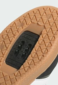 Suola di sneaker in bianco e nero con una suola esterna in gomma testurizzata, dotata di una piastra di ritenzione nera e fori di montaggio doppi per i tacchetti.