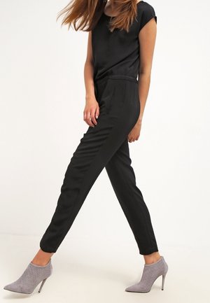 Combinaison noire ajustée à manches courtes et jambes fuselées ; présente une texture douce. Assortie avec des chaussures à talons hauts grises claires à motifs.