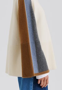 Pull en tricot avec un corps crème à texture côtelée et des manches rayées marron, bleu, gris et gris foncé.