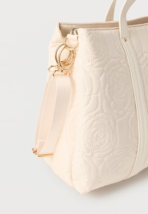 Krēmkrāsas izšūta soma ar ziedu rakstu, zelta metāla riņķiem un regulējamu auduma plecu siksnu, kas pievienota vienai pusei.