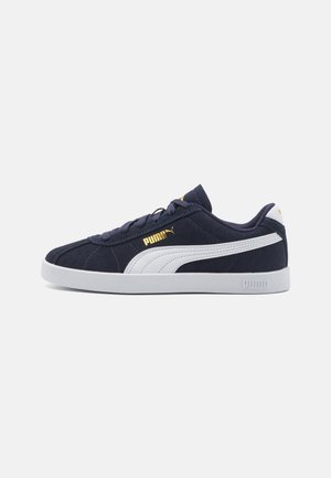 Zapatillas de ante marino con acentos en blanco, punta redonda, suela plana y diseño con cordones. Presenta un logotipo dorado en el lateral y en la lengüeta.
