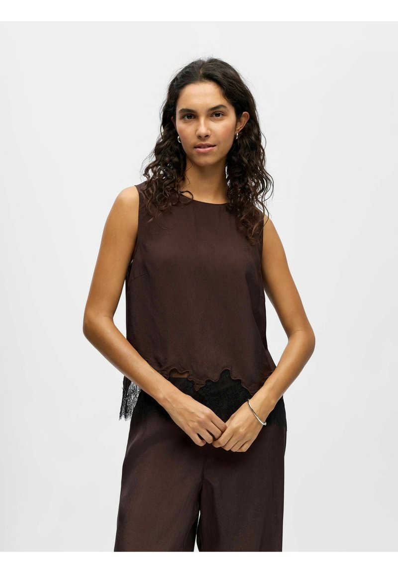 Top marrone senza maniche con orlo scallopato e dettagli in pizzo nero lungo il fondo. Tessuto liscio e vestibilità comoda.
