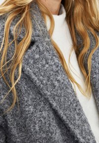 Gray textured knit cardigan with a soft, fluffy finish, showcasing a loose fit and prominent shawl collar, layered over a white top.