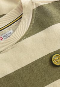 Beige en olijf gestreepte gebreide trui met geribde kraag, genaaide merketiket en een rond geel-zwarte merkbadge op de stof.