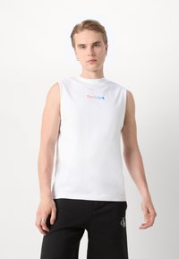 Camiseta sin mangas blanca con el texto multicolor "Esto es Amor" en el pecho. Confeccionada en una tela suave y con un cuello redondo. Corte casual.