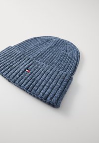 Gorras de punto azul con una textura de canalé y un puño doblado, que presenta una pequeña etiqueta de logotipo en rojo, blanco y azul en el lateral.