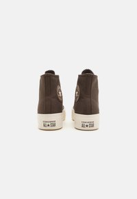 Bruna kanvas högstövlar med vita gummisulor, Converse All Star-logotyp vid ankeln, strukturerad yta och dragflikar bak.