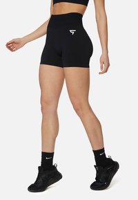Črne športne kratke hlače z visokim pasom, na strani z belim logotipom. Gladka tekstura, prilegajoča zasnova in dolžina do sredine stegen.
