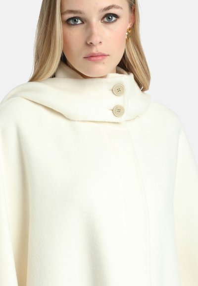Witte wollen cape met een hoge kraag, voorzien van twee lichtbruine knopen. Zachte textuur, minimalistisch ontwerp en geen zichtbare patronen of accenten.
