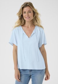 Haut bleu clair à manches courtes avec un col en V, des liens décoratifs et une coupe décontractée. Tissu texturé doux avec un ourlet droit.