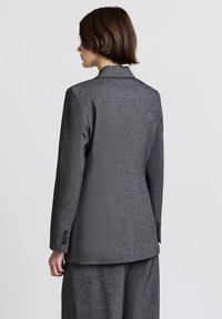 Blazer grigio con texture, design monopetto, rever a lancia e tre bottoni decorativi sui polsini.