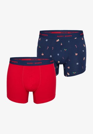 Deux paires de shorts : un rouge uni et un bleu marine avec des motifs festifs de cannes en sucre, d'ornements et de flocons de neige. Les ceintures élastiques sont marquées.