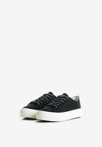 Sneakers neri con dettagli in rilievo, suola bianca testurizzata e lacci neri spessi con accenti bianchi. Punta arrotondata e design a profilo basso.